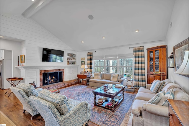 living area with lofted ceiling with beams, built in shelves, recessed lighting, wood finished floors, and a brick fireplace