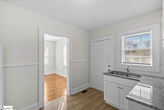 kitchen featuring light wood finished floors, baseboards, visible vents, dark stone counters, and a sink