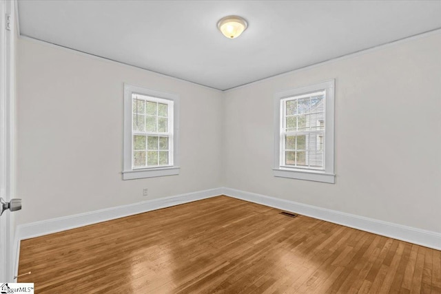 spare room with baseboards, visible vents, and wood finished floors