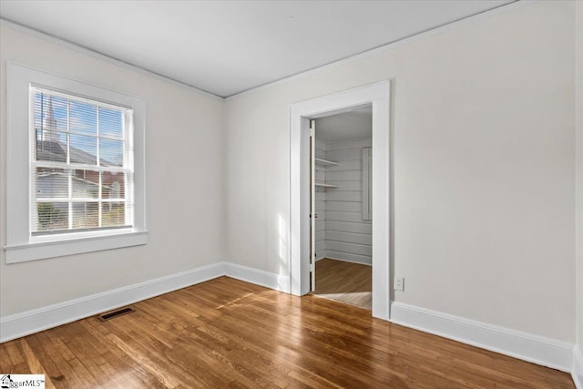 unfurnished bedroom with baseboards, visible vents, a walk in closet, and wood finished floors