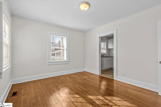 unfurnished bedroom with ensuite bathroom, hardwood / wood-style flooring, a sink, visible vents, and baseboards