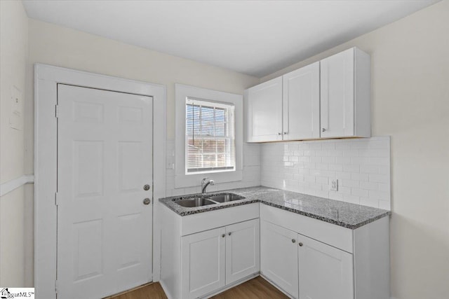 kitchen with wood finished floors, a sink, white cabinetry, tasteful backsplash, and dark stone countertops