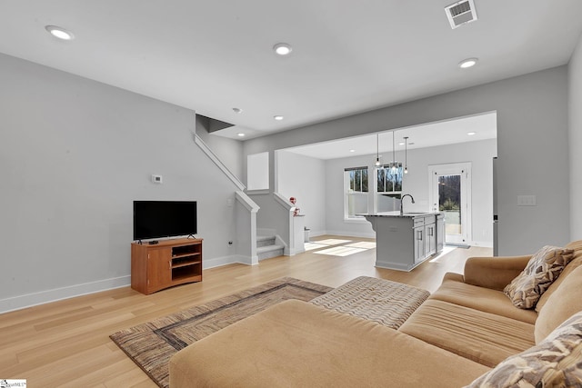 living area with visible vents, baseboards, stairway, light wood-type flooring, and recessed lighting