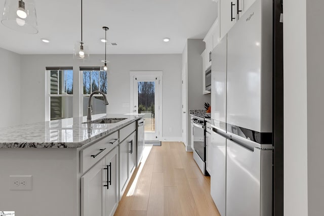 kitchen with a sink, white cabinets, appliances with stainless steel finishes, light wood finished floors, and a center island with sink