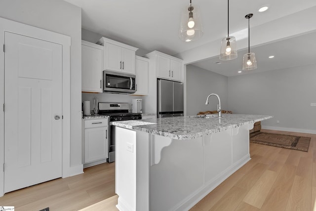 kitchen featuring an island with sink, light wood finished floors, stainless steel appliances, and a sink