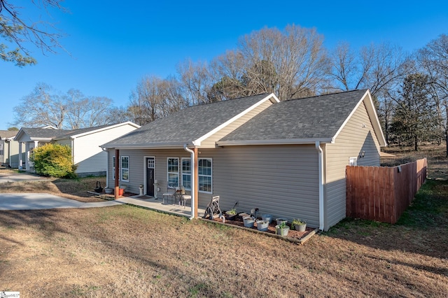 ranch-style house with a front yard, roof with shingles, fence, and a patio