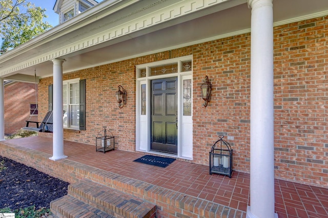 entrance to property featuring a porch and brick siding