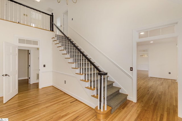 stairs with visible vents, a high ceiling, baseboards, and wood finished floors