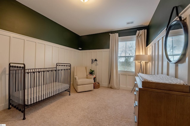 carpeted bedroom with visible vents, a decorative wall, and wainscoting