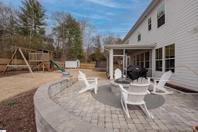 view of patio / terrace with an outdoor fire pit, a storage shed, area for grilling, fence, and a trampoline