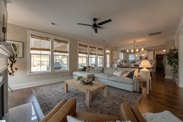 living room featuring visible vents, ornamental molding, dark wood-style flooring, and a glass covered fireplace