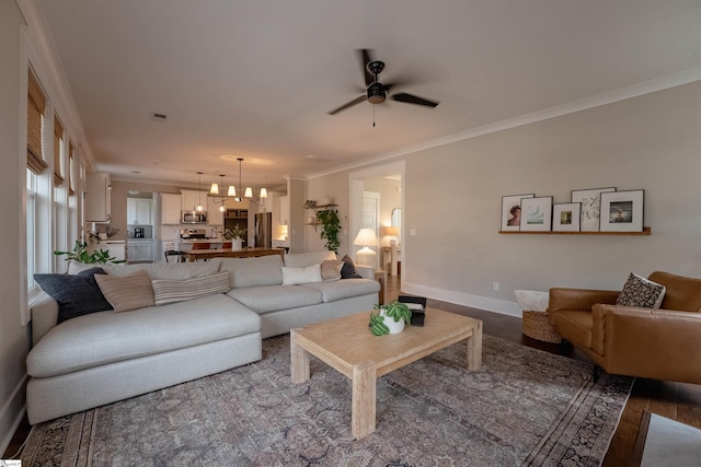 living area featuring ceiling fan with notable chandelier, wood finished floors, visible vents, baseboards, and crown molding