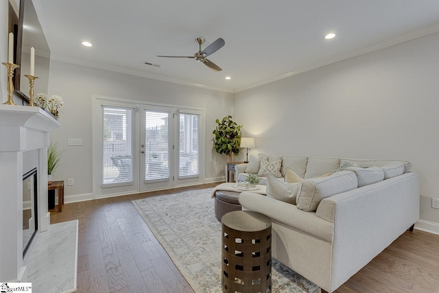 living room with baseboards, visible vents, a premium fireplace, ornamental molding, and wood finished floors