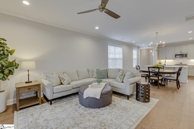 living area with light wood-style floors, recessed lighting, visible vents, and crown molding