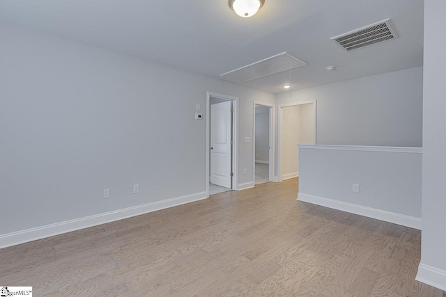 empty room featuring baseboards, attic access, visible vents, and wood finished floors