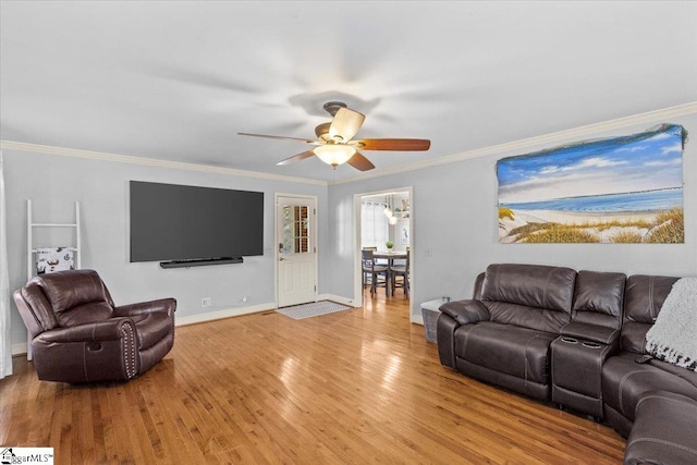 living area featuring light wood-type flooring, baseboards, a ceiling fan, and crown molding