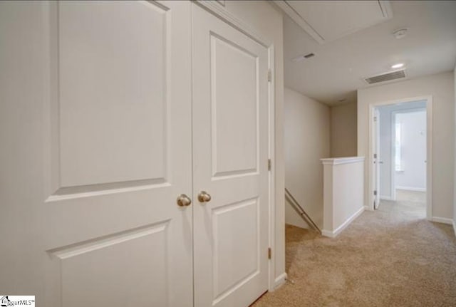 hallway with light colored carpet, visible vents, baseboards, an upstairs landing, and attic access