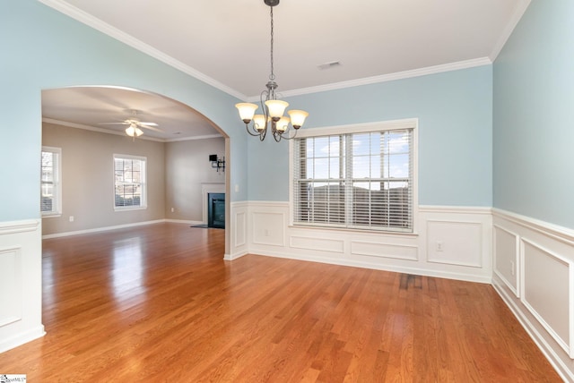 empty room with arched walkways, light wood-style flooring, ceiling fan with notable chandelier, a fireplace with flush hearth, and visible vents