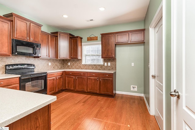 kitchen with black appliances, light wood-style flooring, light countertops, and backsplash