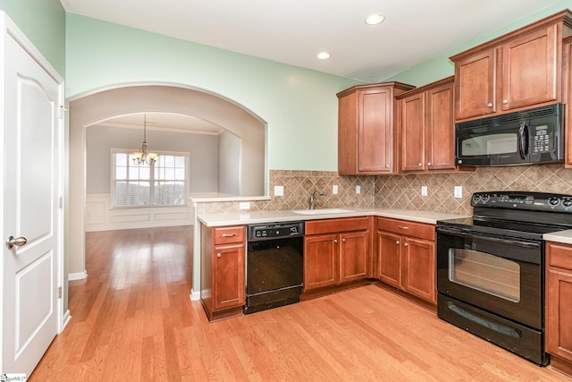 kitchen with a wainscoted wall, brown cabinetry, a sink, light wood-type flooring, and black appliances