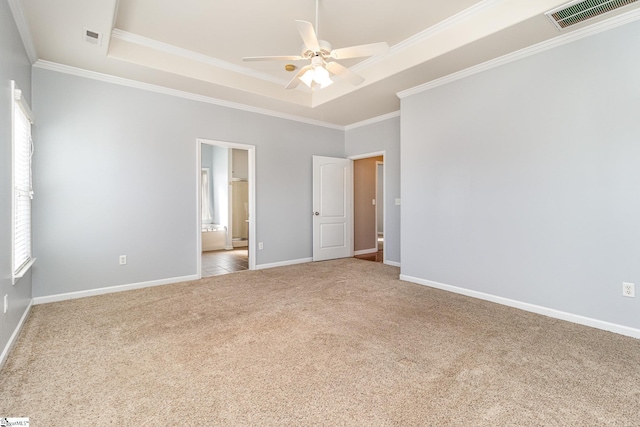 unfurnished bedroom with ornamental molding, a tray ceiling, carpet flooring, and visible vents