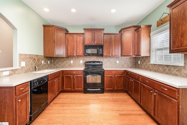 kitchen featuring brown cabinets, backsplash, light wood-style flooring, a sink, and black appliances