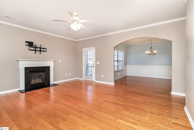 unfurnished living room with light wood finished floors, arched walkways, a glass covered fireplace, crown molding, and ceiling fan with notable chandelier