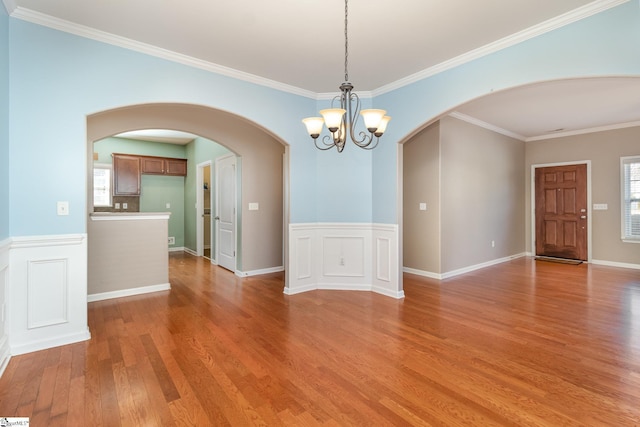 unfurnished room with light wood-type flooring, a wainscoted wall, and arched walkways