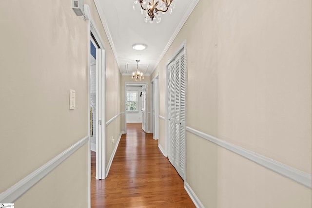 hallway featuring baseboards, ornamental molding, wood finished floors, and an inviting chandelier