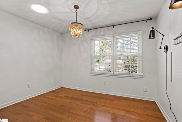 unfurnished room featuring a notable chandelier, baseboards, and wood finished floors