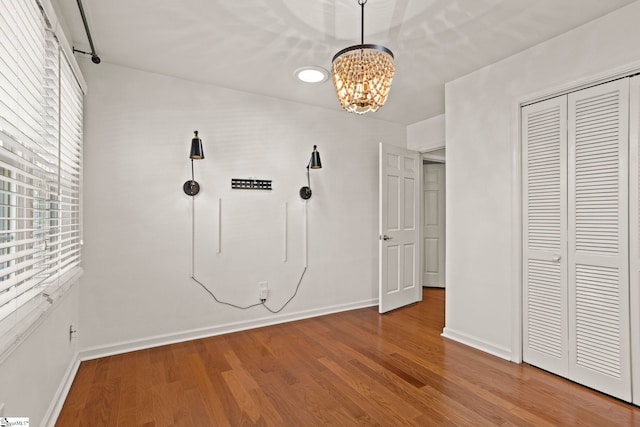 unfurnished bedroom featuring baseboards, a closet, wood finished floors, and a notable chandelier