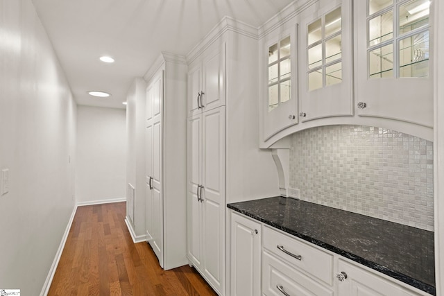 interior space with baseboards, decorative backsplash, glass insert cabinets, dark wood-style flooring, and white cabinetry