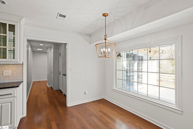 unfurnished dining area featuring a chandelier, dark wood-type flooring, visible vents, baseboards, and ornamental molding