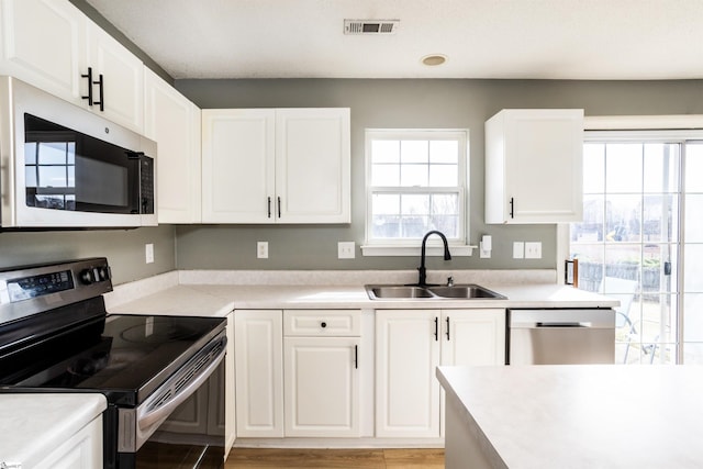 kitchen featuring stainless steel appliances, light countertops, visible vents, white cabinets, and a sink