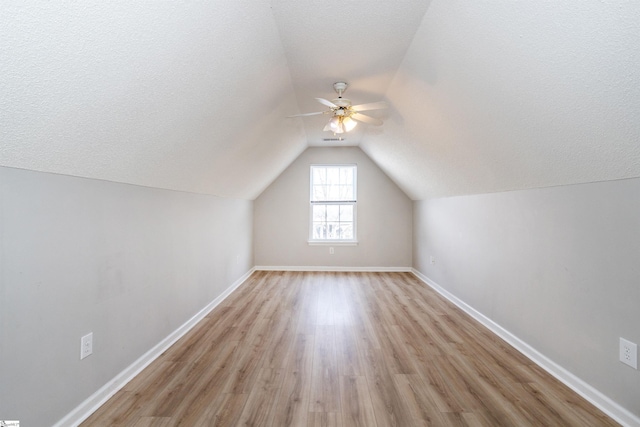 bonus room featuring lofted ceiling, light wood-style floors, ceiling fan, a textured ceiling, and baseboards