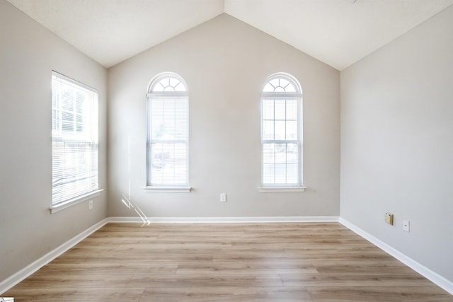 spare room with lofted ceiling, a healthy amount of sunlight, and light wood finished floors