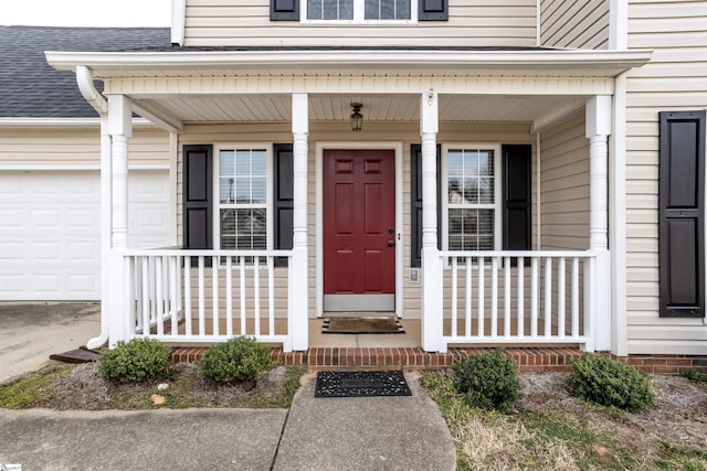 view of exterior entry featuring a garage, a shingled roof, and a porch