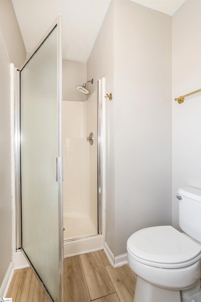 bathroom with toilet, a stall shower, baseboards, and wood finished floors