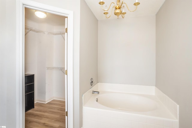 bathroom with a garden tub, a notable chandelier, a walk in closet, and wood finished floors