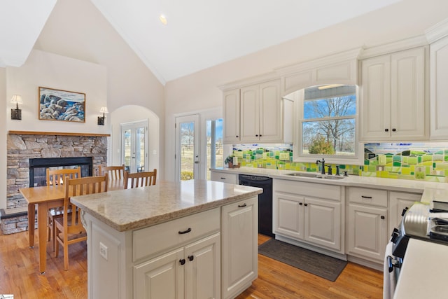 kitchen with a stone fireplace, a sink, stainless steel electric range, light wood-type flooring, and dishwasher