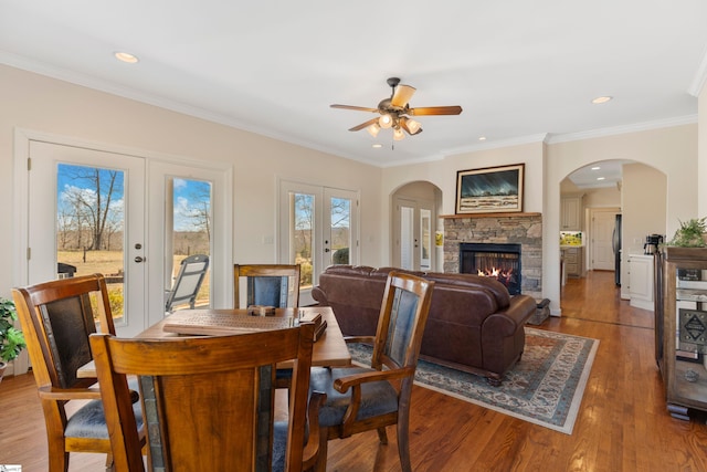 dining room with wood finished floors, ornamental molding, a stone fireplace, and french doors