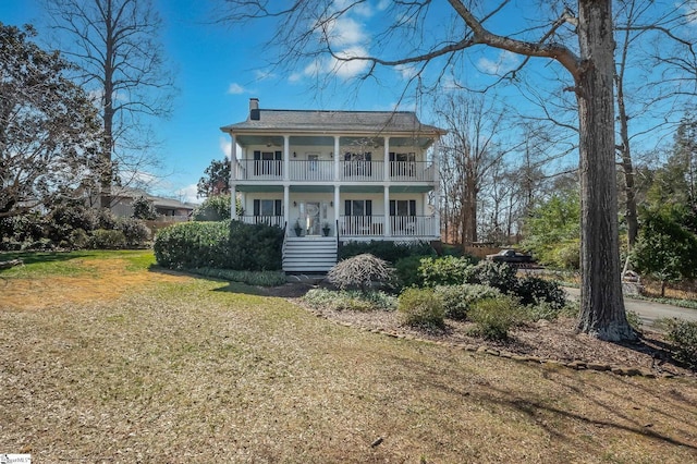 view of front facade with a porch, a chimney, a front yard, and a balcony