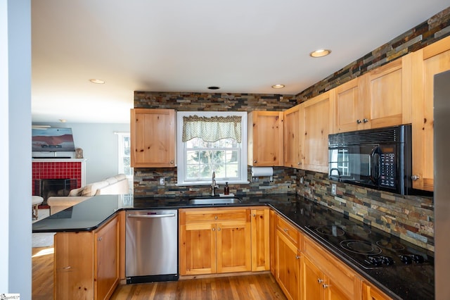 kitchen featuring a fireplace, decorative backsplash, a sink, a peninsula, and black appliances