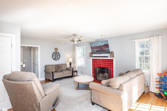 living room with a tile fireplace, ceiling fan, baseboards, and wood finished floors