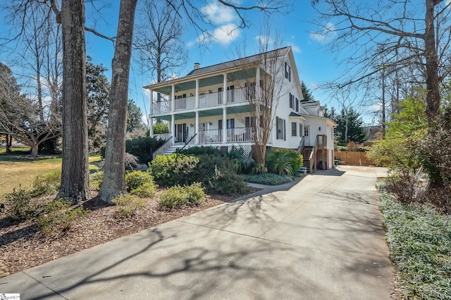 view of front of property featuring covered porch, concrete driveway, a chimney, and a balcony