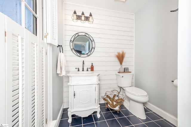 bathroom featuring toilet, wood walls, vanity, baseboards, and tile patterned floors