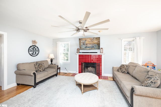 living room with baseboards, ceiling fan, a tiled fireplace, and wood finished floors