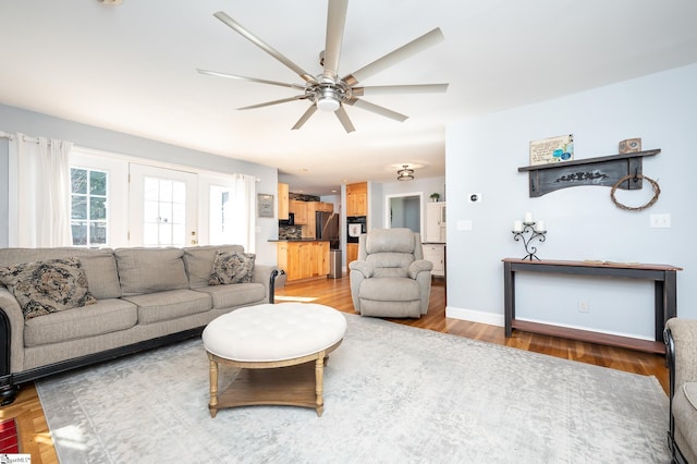 living room featuring light wood finished floors, ceiling fan, and baseboards