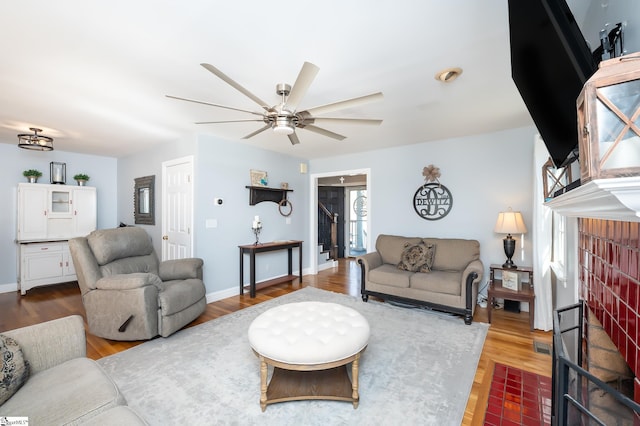 living area featuring a fireplace, wood finished floors, a ceiling fan, and baseboards