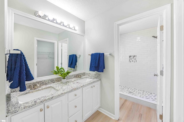 bathroom with a textured ceiling, wood finished floors, a stall shower, and a sink